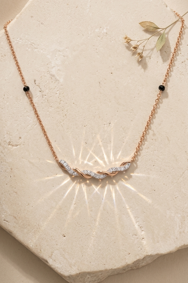A delicate rose gold necklace with a central cluster of clear pavé stones and small black bead accents, displayed on a textured beige stone surface with a soft starburst light effect.